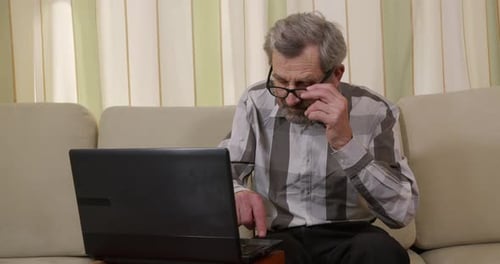 Senior Man Using Laptop at Home on Sofa