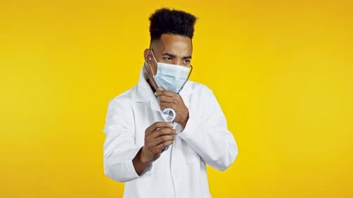 Portrait of Serious African Doctor in Medical Coat and Mask Using Stethoscope Isolated on Yellow