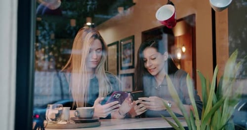 Two Young Womans Using Mobile Phone in Cafe