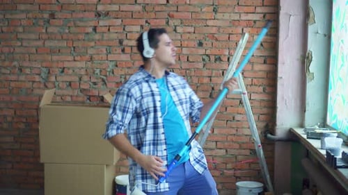 an Expressive Cheerful Man in a Shirt and Headphones During the Repair Plays an Imaginary Guitar