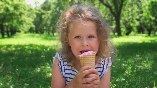 Cute blonde curly girl eating ice cream in the park on a sunny summer day.