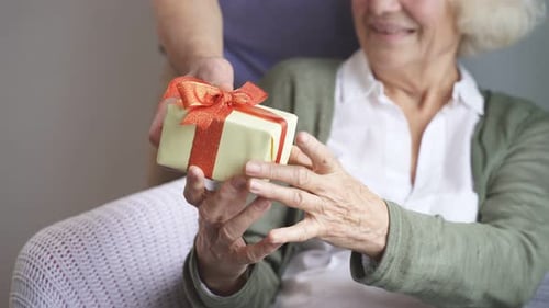 Adult Gives Gift to Smiling Senior Woman