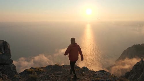 Silhuette of Young Man Arms Outstretched Observing Beautiful Dramatic Colorful Sunset Above a Sea