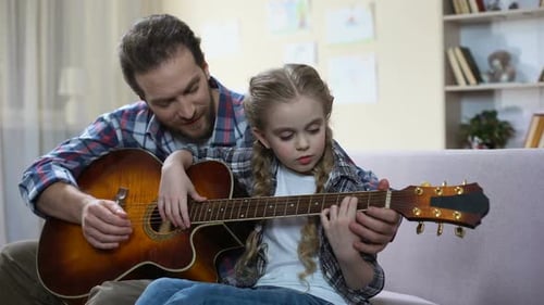 Man Teaches Child to Play Guitar Indoors