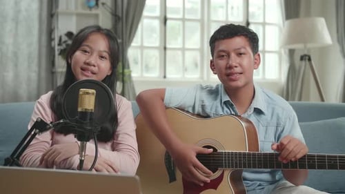 Chico asiático con guitarra y chica hablando con la cámara. The Children está transmitiendo en vivo