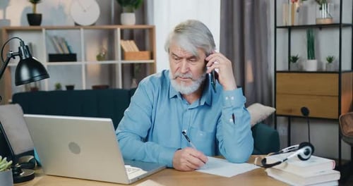 Alter Mann schaut auf den Computerbildschirm, während er auf dem Handy spricht