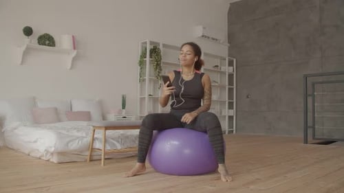 Woman Bounces on Exercise Ball, Listening to Music