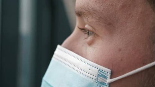 Close up man in face mask looking through window into the distance.