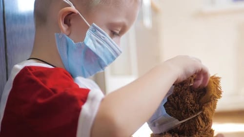 Young Child Carefully Puts Mask on Teddy Bear