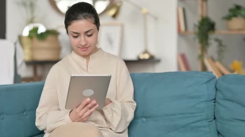 Woman Using Tablet on Teal Couch Indoors