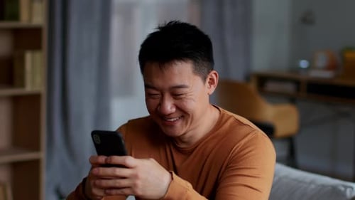 Man Laughing While Looking at Mobile Phone Indoors