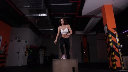 Beautiful Fitness Athlete Performs Box Jumping in the Gym in a White Sports Top