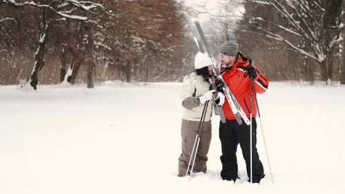 Casal, homem e mulher idosos, caminham com bastões de esqui e olham em volta curtindo a natureza na floresta