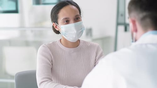 Young Woman in Medical Mask Speaking with Doctor in Clinic