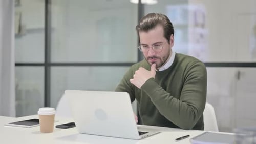 Young Businessman Thinking While Working on Laptop in Office