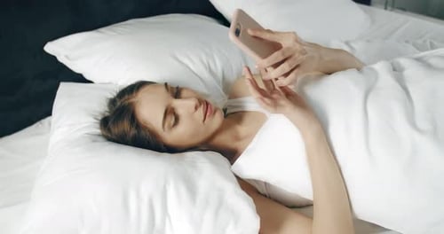 Woman Smiling Using Mobile Phone in Bed
