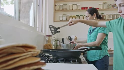 Boy preparing pancakes with his mother for breakfast in the kitchen