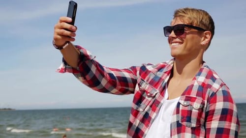 Hombre con smartphone tomando selfie en la playa de verano
