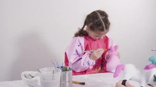 Child Carefully Painting Ceramic Figures with Help