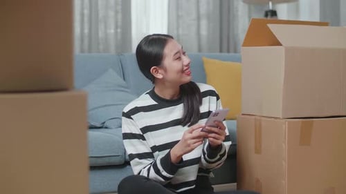 Woman Using Smartphone Surrounded by Moving Boxes