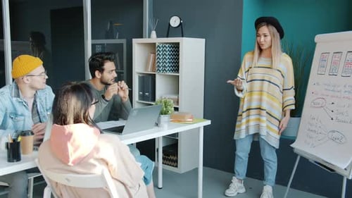Creative Young Designer Talking to Teammates Discussing New Project Making Presentation in Office