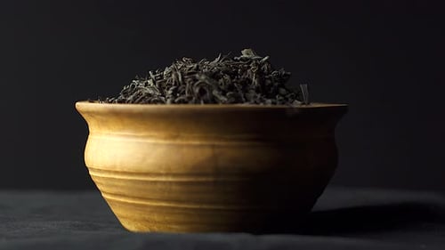 Close up view dry black ceylon tea leaves rotate in a clay bowl on black background