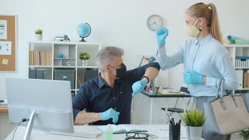 Man and Woman in Face Masks Office Workers Doing Elbow High-five at Work During Pandemic