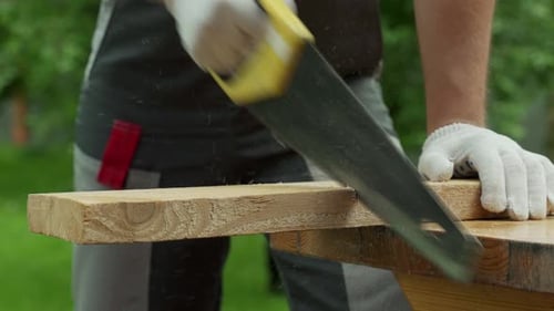 Man Carpenter Saws a Wooden Board with a Hand Saw