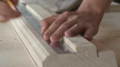 Craftsman Measures Wooden Piece with Ruler and Pencil
