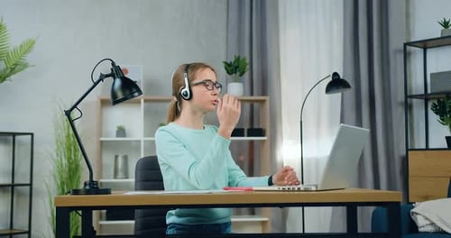 Mujer independiente con gafas sentada frente a la computadora en casa y realizando una videoconferencia