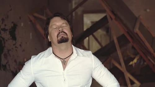 Retrato de um jovem brutal com barba fica em uma sala destruída e amassa o pescoço de perto