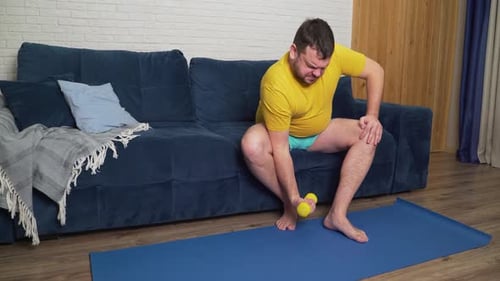 Man Lifts Small Dumbbell With Difficulty at Home