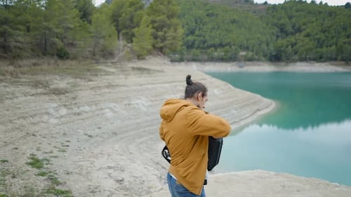 Un jeune homme sort un appareil photo de son sac à dos et photographie un lac en Espagne