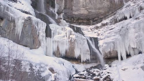 Wunderschöner Wasserfall im Winter mit Eiszapfen links und rechts, die eine atemberaubende gefrorene Szene schaffen - dolly i