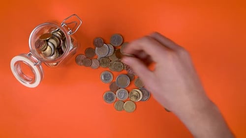 Hand Placing Euros Into a Glass Jar