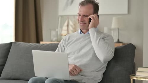 Adult Talking on Phone with Laptop Indoors