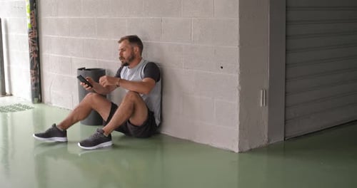 Man Ties Shoes, Looks at Phone in Urban Space