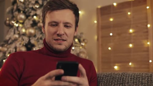 Man with Phone Smiling Near Christmas Tree