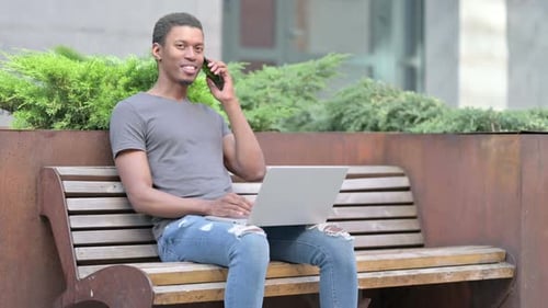 Man Using Laptop and Smartphone on Bench