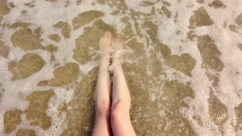 Female Legs in the Waves of the Sea Surf.