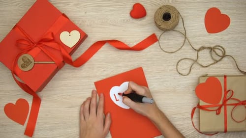 Writing Love Card with Gifts and Hearts Overhead