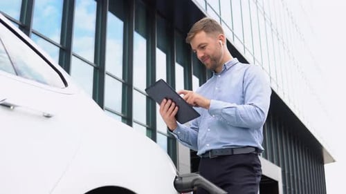Man Using Tablet While Charging Electric Car