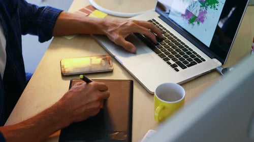 Person Uses Tablet, Pen, and Laptop at Desk