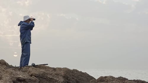 Old fisherman looking into the ocean using his binoculars