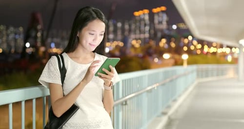 Young Woman Using Smartphone on Pedestrian Bridge at Night