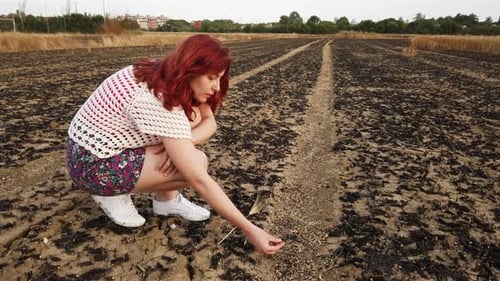 Woman Kneeling in Charred Rural Field