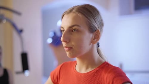 Headshot of Positive Confident Caucasian Sportswoman Stretching Neck Muscles in Gym with Blurred