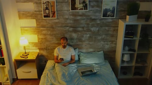 Man Using Smartphone in Cozy Bedroom at Night