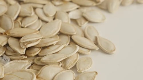 Close-up pepitas on pile slow tilt 4K 2160p 30fps UltraHD footage - Raw pumpkin seed on white 3840