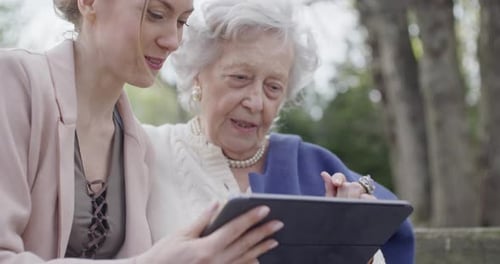 Woman and Senior Grandmother Using Tablet Device for Video Call at Park